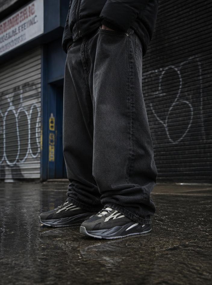 Baggy STRIVE jeans stacked over sneakers on wet asphalt